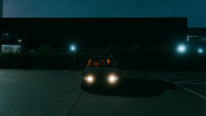 Car with headlights on in dark parking lot at night