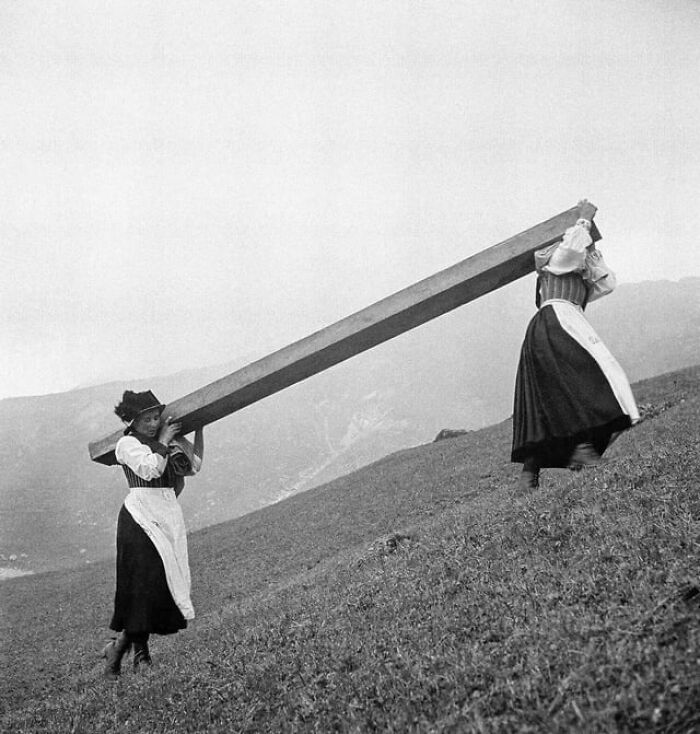 Historical photo of two women carrying a long wooden beam on a hillside showing charming moments