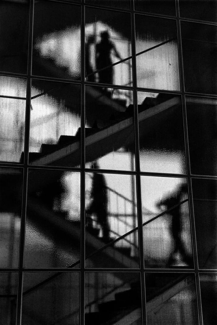 Silhouettes of people walking on staircase behind textured glass window in black and white