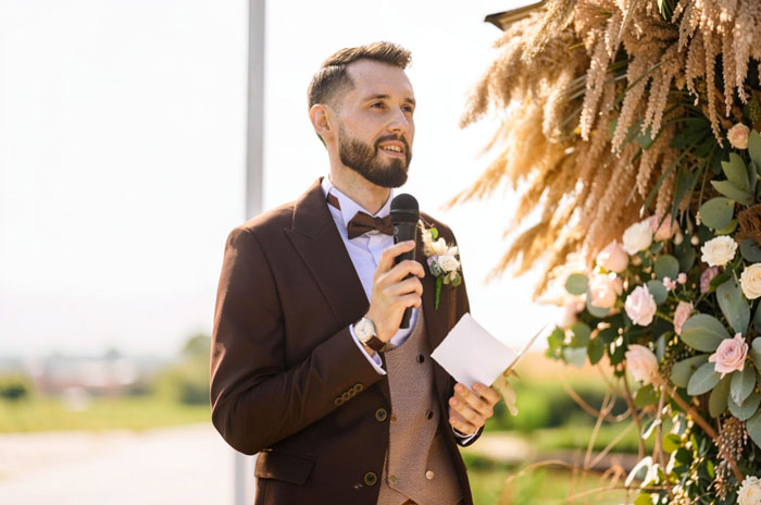 A groom holding a microphone, making an important announcement to a room full of witnesses.