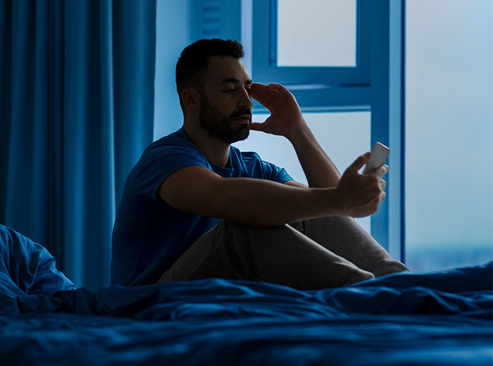 Man sitting on bed looking stressed holding phone at night about wife's affair partner Man sitting on bed looking stressed holding phone at night about wife's affair partner