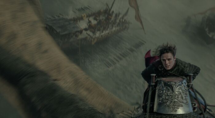 A man rides a dragon over a stormy sea with ships below, part of a brutal naval clash in House of the Dragon. A man rides a dragon over a stormy sea with ships below, part of a brutal naval clash in House of the Dragon.