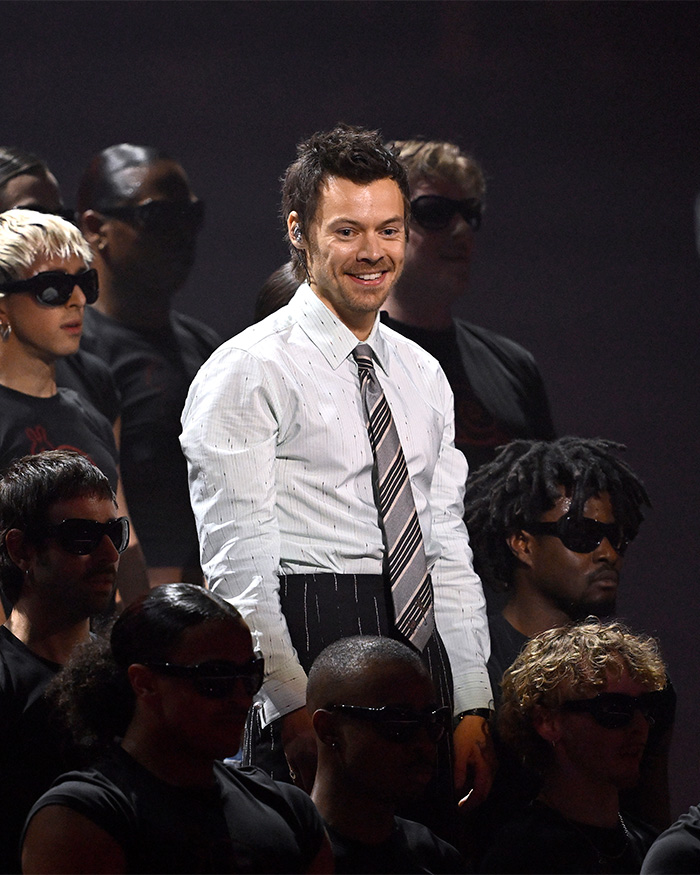 Harry Styles onstage, smiling despite later choking on water and collapsing during scorching heatwave.