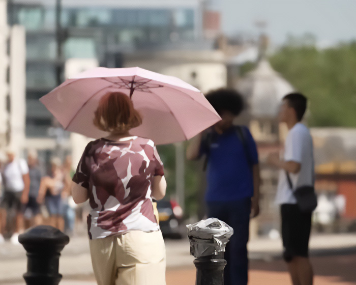 A person using a pink umbrella for shade during a scorching heatwave.