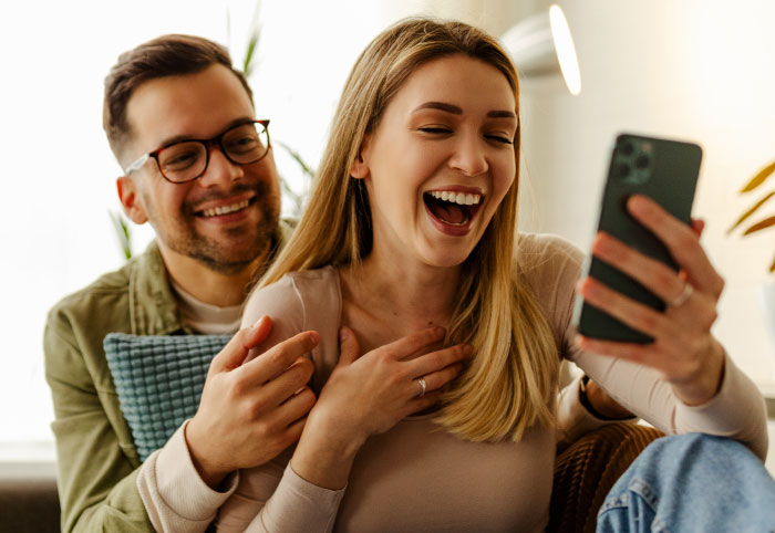 A happy couple looking at a phone, symbolizing things partners never tell each other.