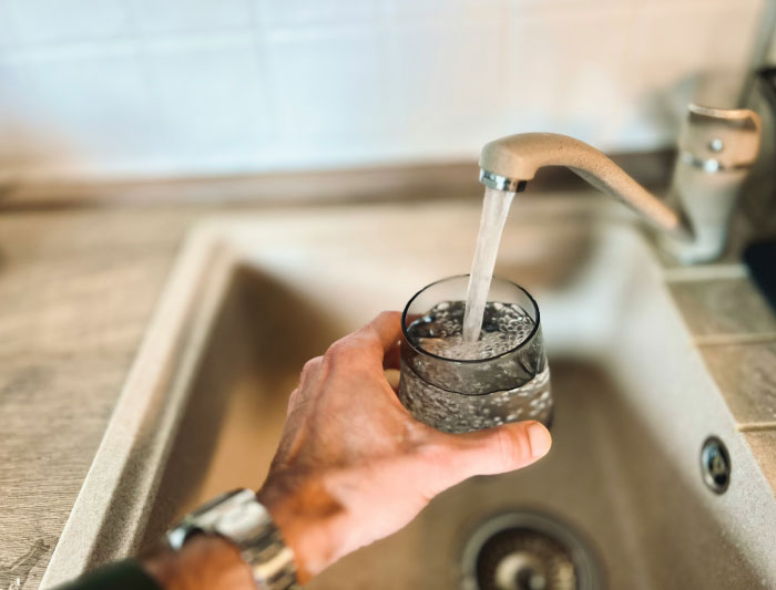 A hand filling a glass with water from a kitchen faucet, symbolizing things people never tell their partners.