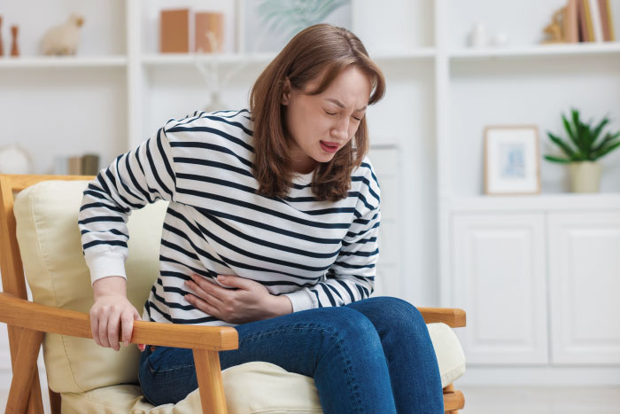 A woman sitting on a chair, holding her stomach in pain. People tell their partners everything but will never tell these things.