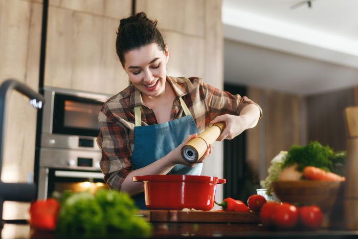 A woman happily seasoning food in a kitchen. People tell their partners everything but will never tell these things.