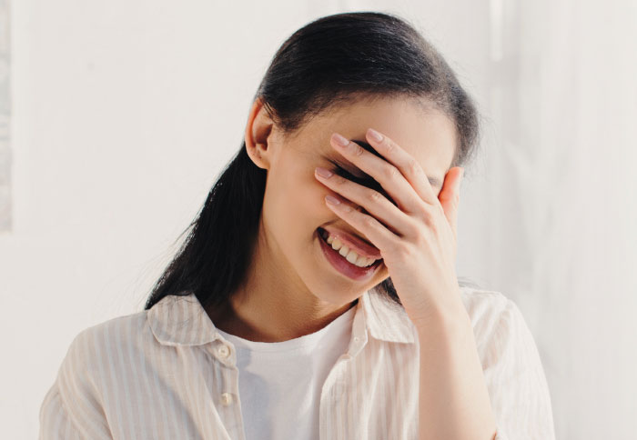 A woman covering her face while laughing, illustrating private things partners never tell.