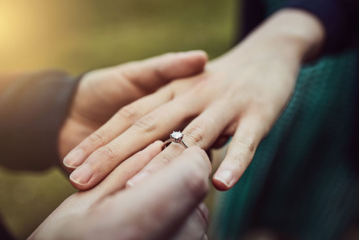 A man placing an engagement ring on a woman's finger, symbolizing things partners will never tell.