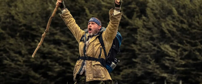 Brad Pitt raising stick victoriously in survival gear outdoors Brad Pitt raising stick victoriously in survival gear outdoors