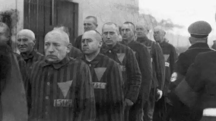 Historical photos: A line of men in striped uniforms with triangular badges on their chests, some looking forward.