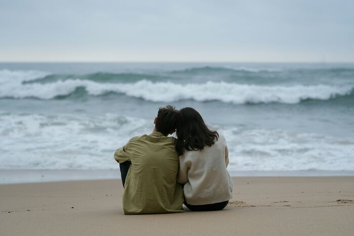 A couple sits on a beach, gazing at the ocean waves, symbolizing one of the useless facts that are hard to forget.