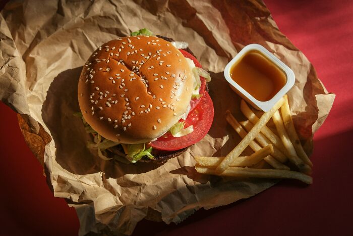 Burger, fries, and dipping sauce on paper showing generosity in food presentation