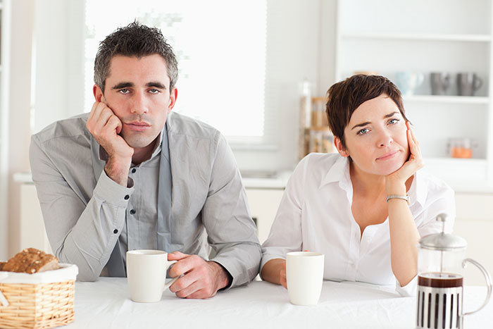 A disheartened couple sits at a table, reflecting the regrets of an open marriage and impending divorce. A disheartened couple sits at a table, reflecting the regrets of an open marriage and impending divorce.