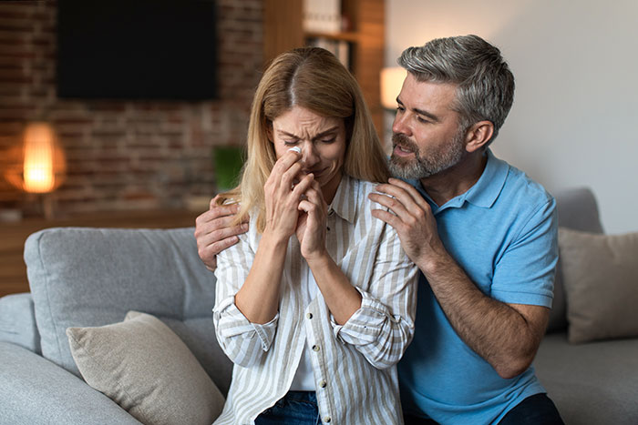 A man comforts a crying woman on a sofa. He regrets open marriage to avoid divorce. A man comforts a crying woman on a sofa. He regrets open marriage to avoid divorce.