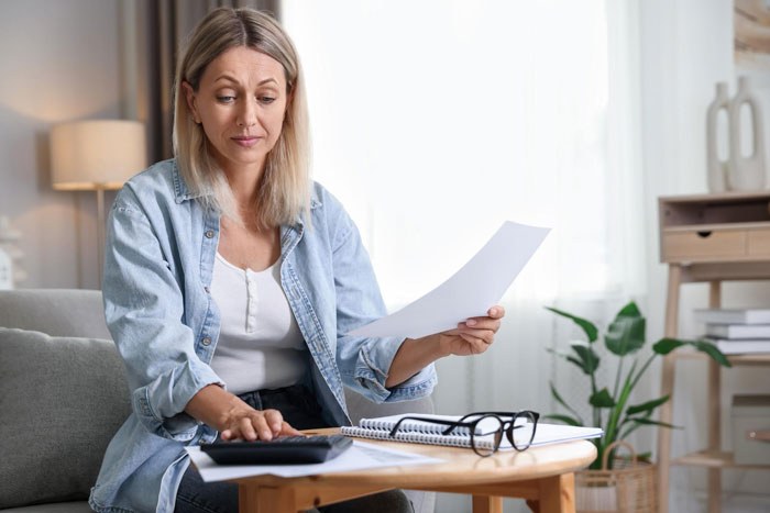A woman looking at documents and calculating with a calculator, wondering if she owes his GF anything from an inheritance.