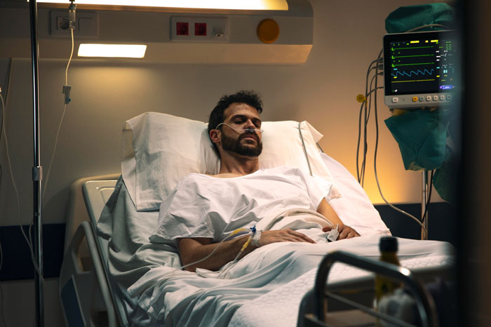 A man lies in a hospital bed, receiving medical care, part of the Guy&rsquo;s final apology and inheritance story.