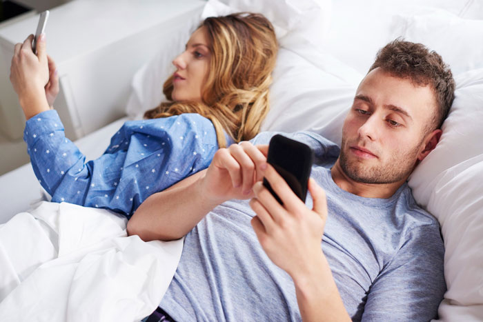 Couple lying in bed distracted by their phones, related to husband phone revealing generated photos
