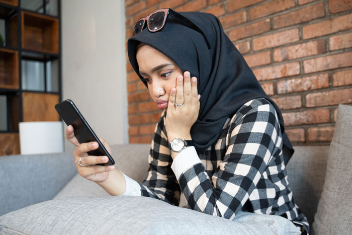 Woman in hijab looking worriedly at phone, revealing husband phone generated photos issue
