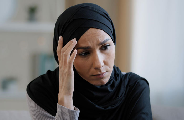 Worried woman in hijab reflecting on husband phone revealing generated photos