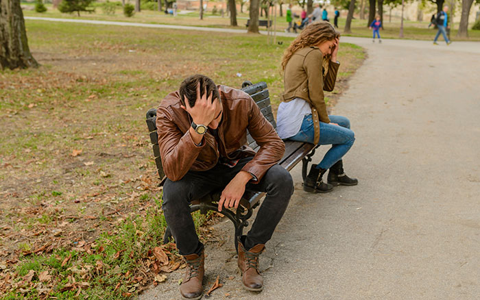 Distraught man on a park bench, woman in the background. Reflects a wife's wits' end due to a broken postnup promise. Distraught man on a park bench, woman in the background. Reflects a wife's wits' end due to a broken postnup promise.