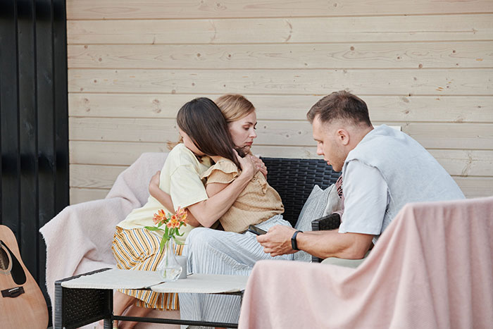 A wife at her wits end, comforted by another woman, while the husband looks on, considering their marriage. A wife at her wits end, comforted by another woman, while the husband looks on, considering their marriage.