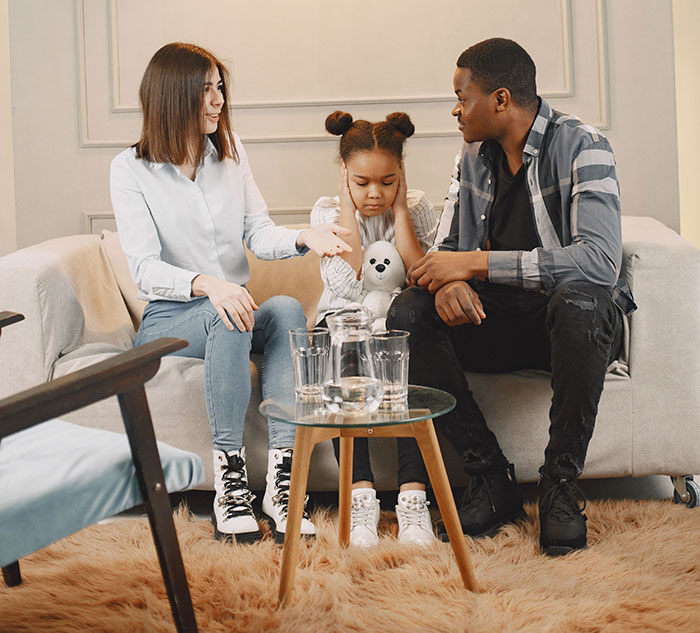 A couple and their child sitting on a sofa, the child covering her ears. The wife is at her wits' end after years of marriage. A couple and their child sitting on a sofa, the child covering her ears. The wife is at her wits' end after years of marriage.