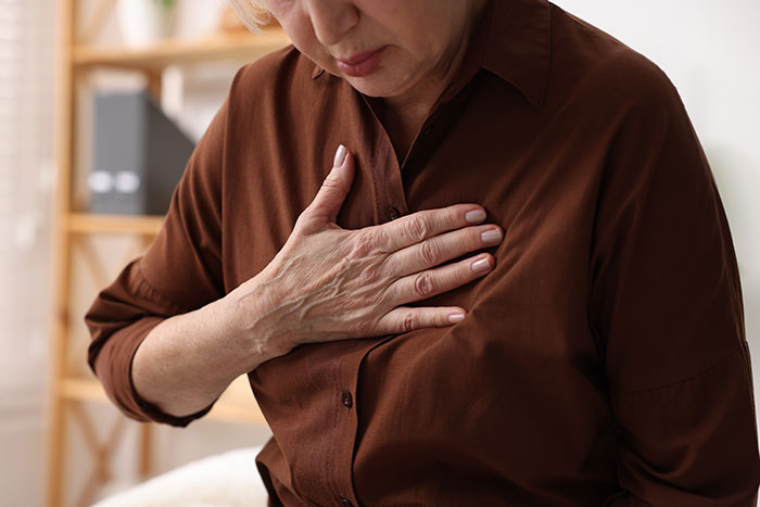 An older woman clutching her chest in pain, highlighting medical symptoms doctors wish people would stop ignoring.