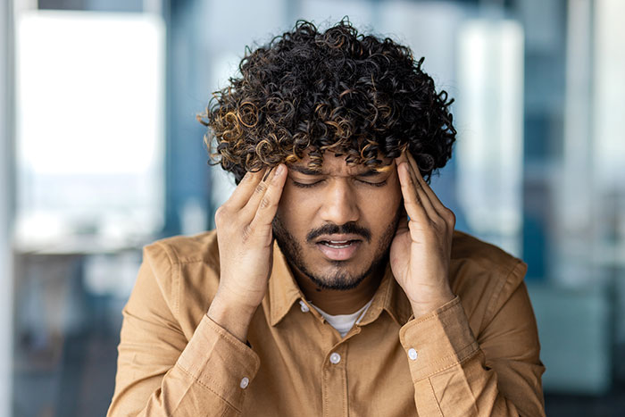 A man with a headache, hands pressed to his temples, illustrating medical symptoms doctors wish people would stop ignoring.