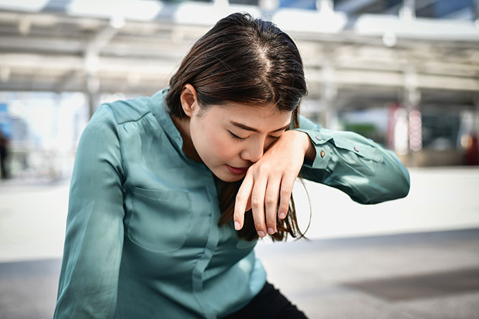 A woman looking unwell, holding her head, symbolizing ignored medical symptoms.