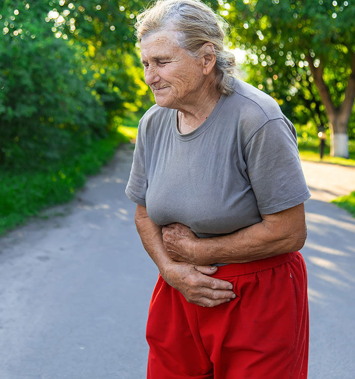 An elderly woman holding her stomach in pain, a medical symptom that should not be ignored as people get older.