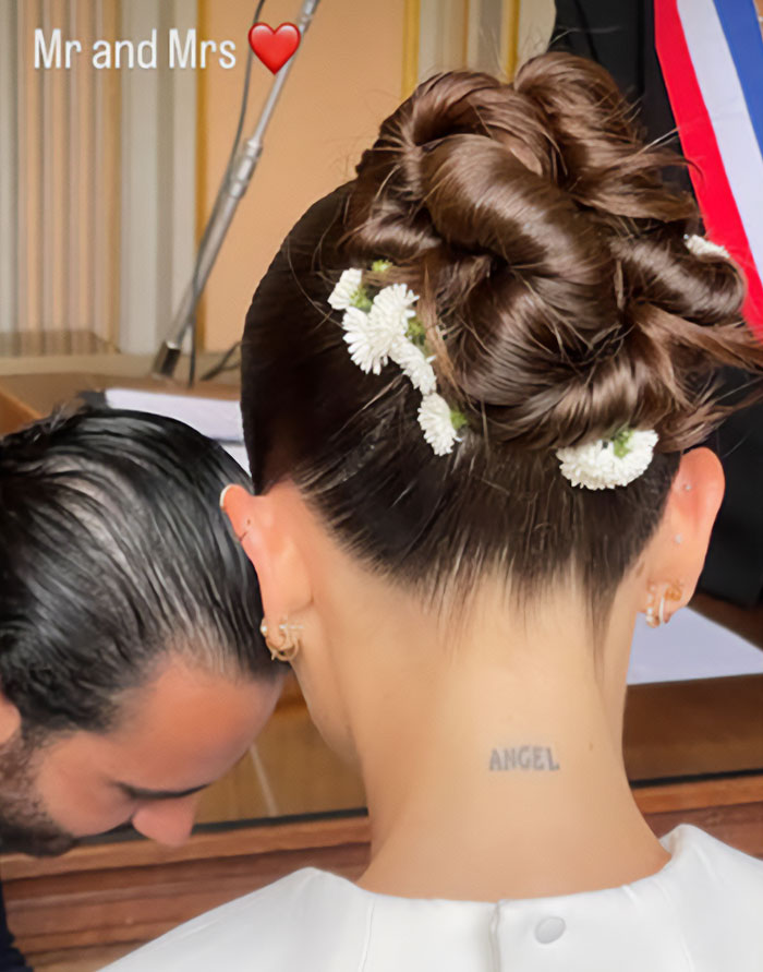 Close-up of Thylane Blondeau's wedding hairstyle with white flowers and a neck tattoo that reads 'ANGEL'.