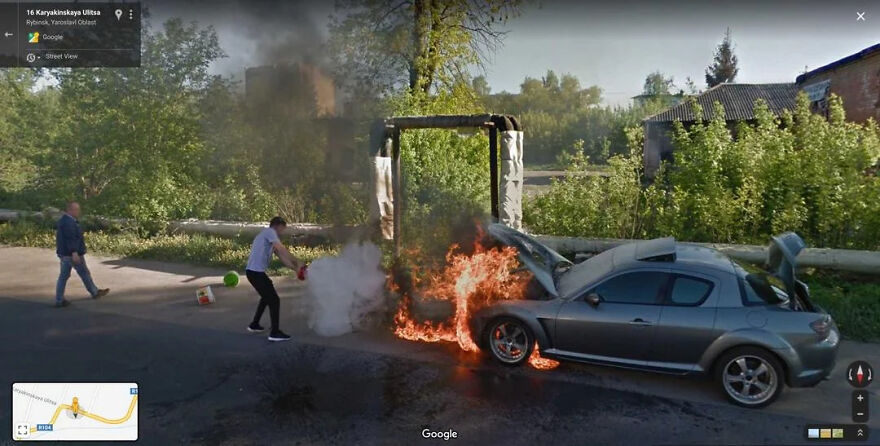 A funny Google Street View photo of a car on fire with a person trying to extinguish it, another man walking away.
