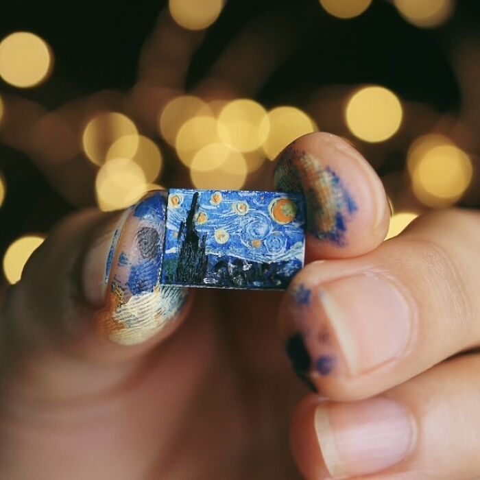 Artist creates miniature paper figures, a miniature rendition of Van Gogh's Starry Night held by paint-stained fingers.