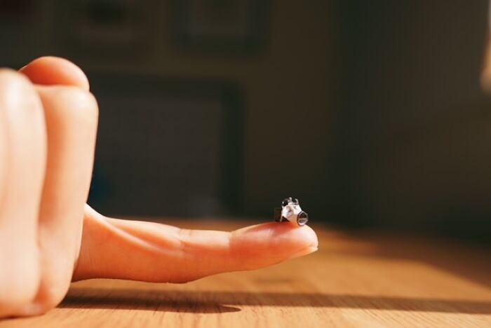 A tiny, detailed miniature paper figure of a camera rests on a person's outstretched finger.