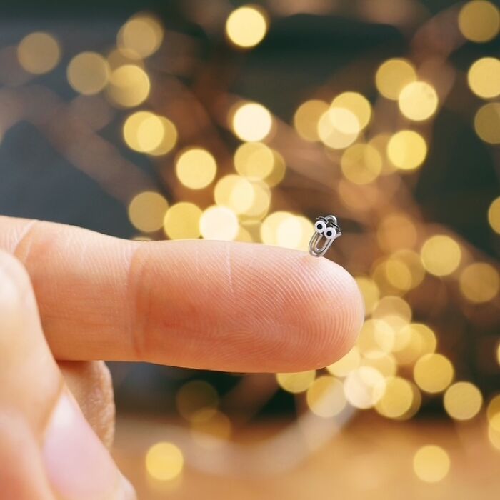 A person's fingertip holds a tiny, detailed miniature paper figure with googly eyes, bokeh lights in background.