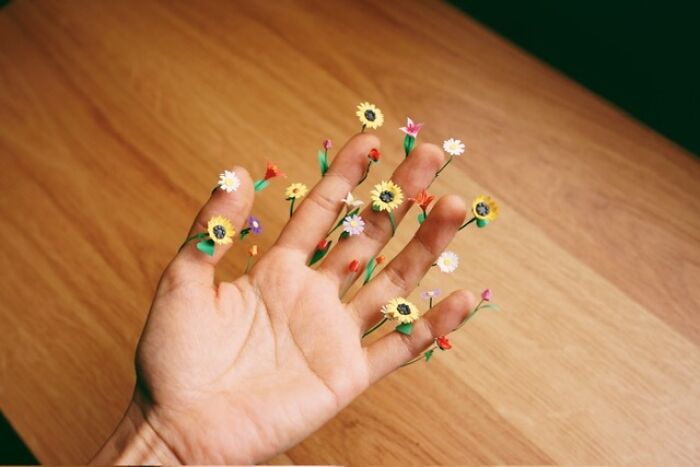 An open hand with many miniature paper figures of colorful flowers blooming from each fingertip.