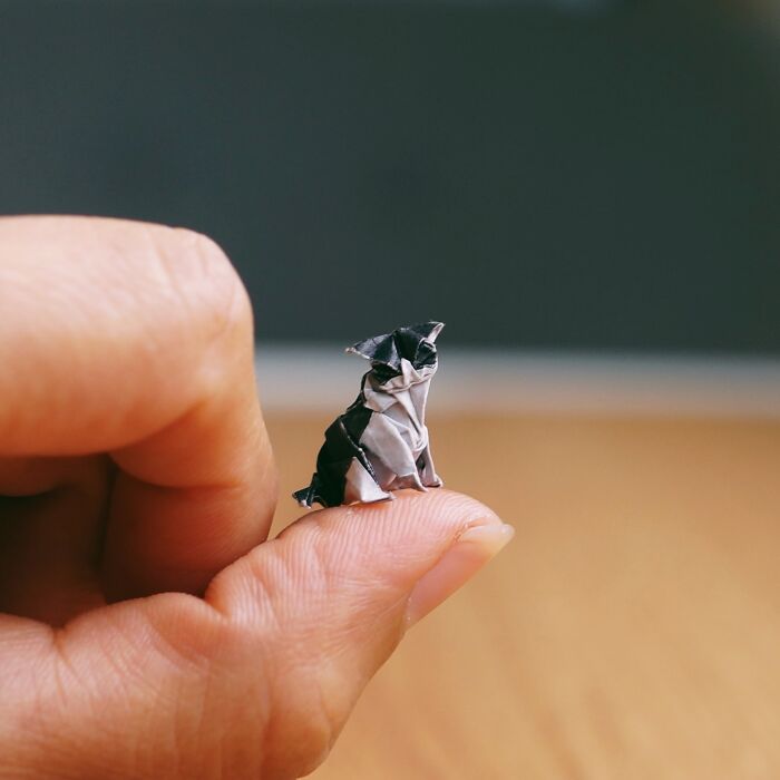A tiny, detailed miniature paper figure of a black and white dog sits on a person's fingertip.