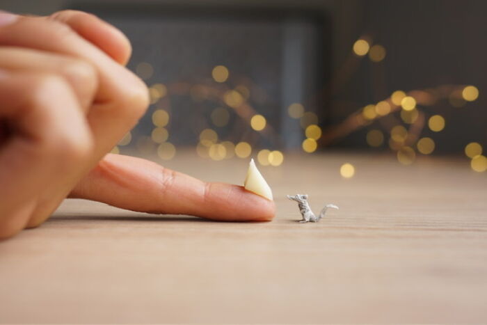 A finger with a tiny cheese-like paper figure next to an even smaller detailed paper mouse.