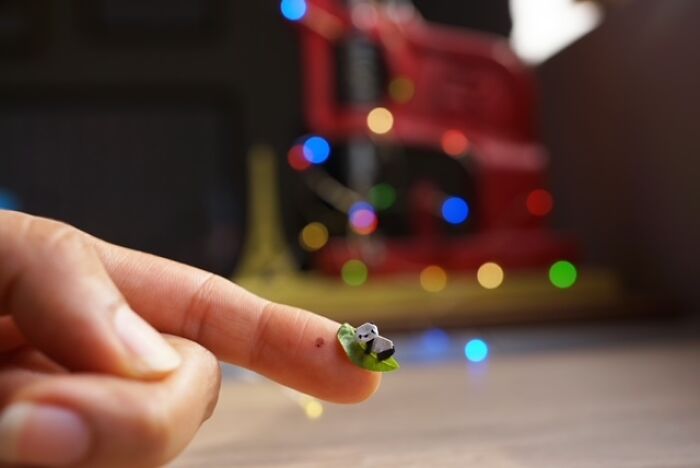 A finger holding a tiny paper panda figure on a small green leaf, illustrating immense detail.