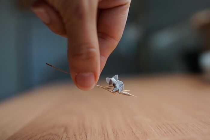Hand gently holding a delicate, tiny miniature paper figure of an animal on a dry twig.