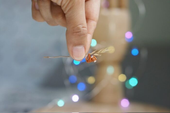 A hand delicately holding a tiny, intricately detailed miniature paper figure of a bird perched on a twig.
