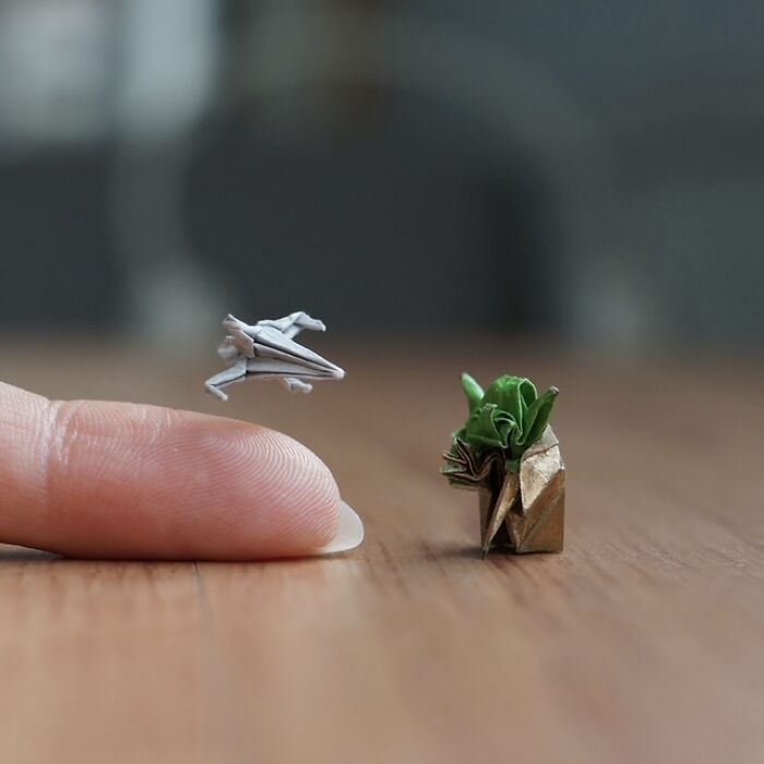 Miniature paper figures: A tiny origami spaceship flying near an origami Yoda on a wooden surface, highlighting immense detail.