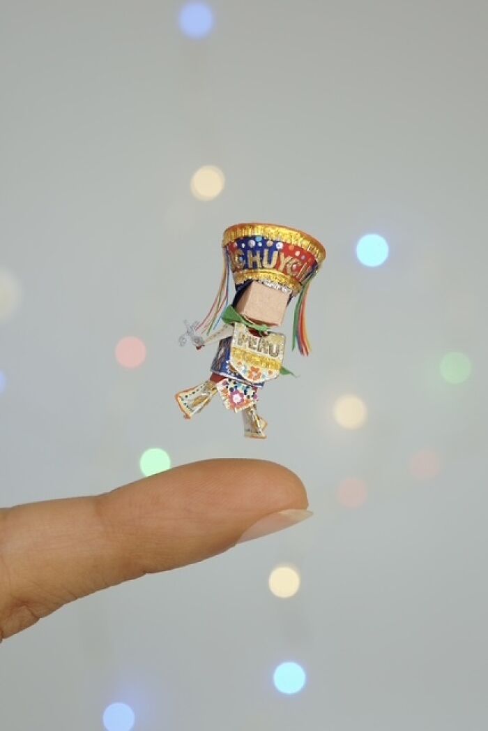 Colorful miniature paper figure with detailed Peruvian attire balanced on a fingertip.