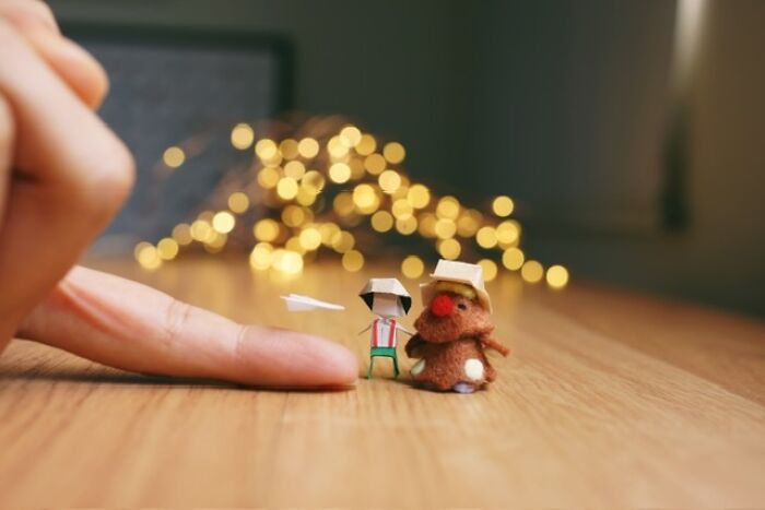 Artist creates miniature paper figures of a paper person and a tiny brown creature, next to a finger, with immense detail.
