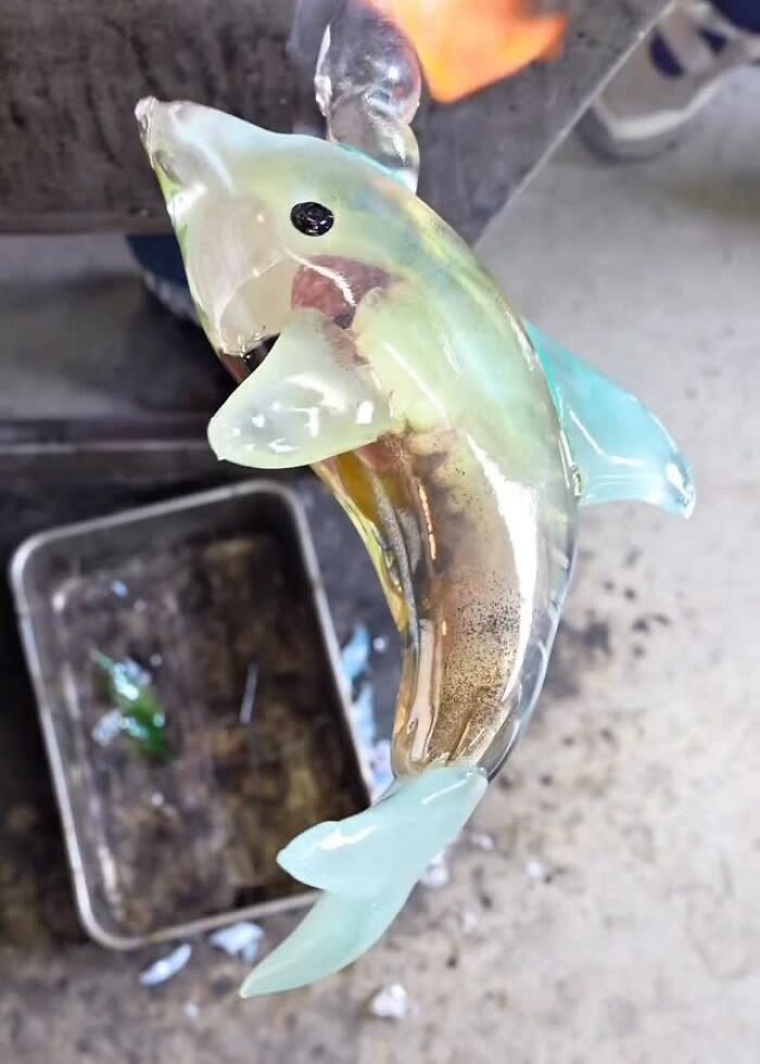 Japanese artist shaping hyper-realistic glass food, a dolphin, with a torch.