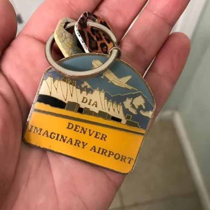 A hand holds a keyring for Denver Imaginary Airport (DIA), representing chaotic airports.
