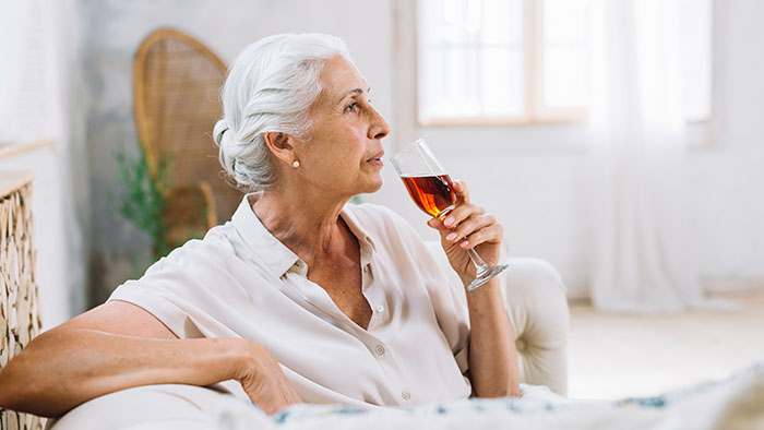 Older woman drinking wine thoughtfully indoors