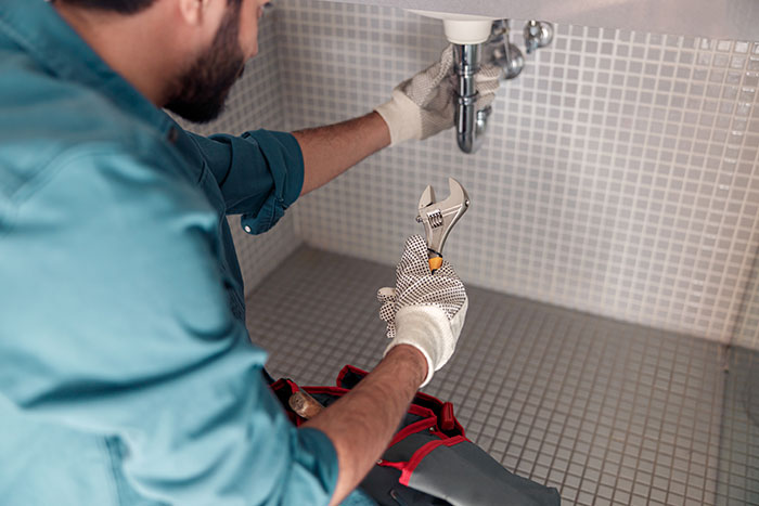 A plumber works under a sink, holding a wrench. Industry secrets customers were never meant to hear.